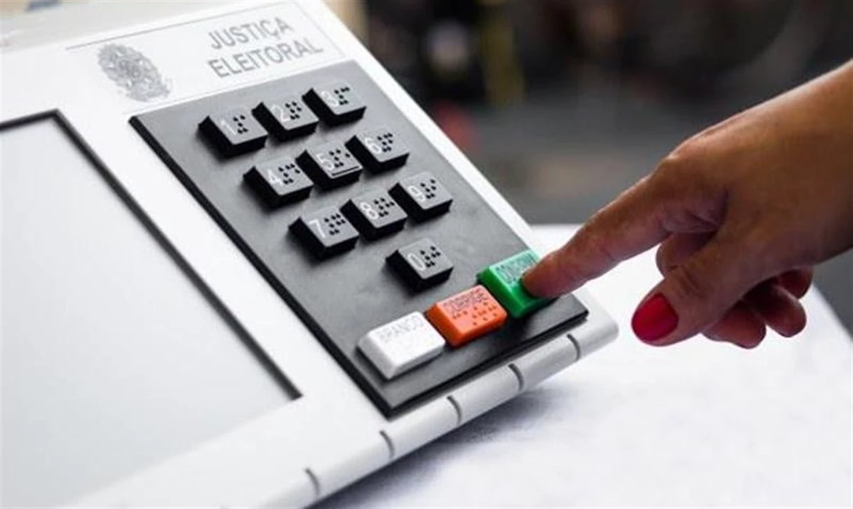 Mão pressionando o botão confirma em uma urna eletrônica da Justiça Eleitoral
